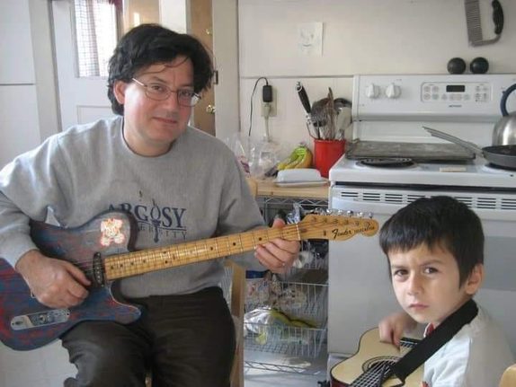 Mark Brunke of Rendition playing electric guitar in a kitchen with a boy also holding a guitar