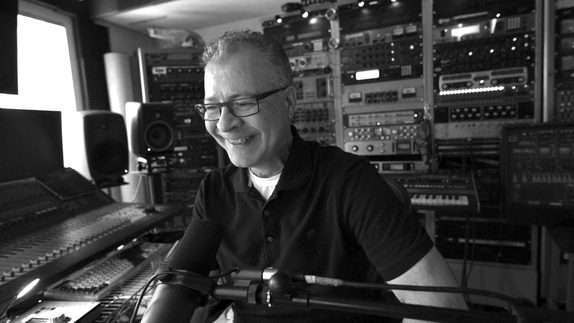 Jerry Hammack of Throttle Body M/C smiling in his recording studio, surrounded by racks of outboard gear